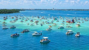 Un port de plaisance où sont amarrés de nombreux bateaux, avec une eau turquoise et limpide, et où l’on aperçoit, au loin, la silhouette d’une ville.