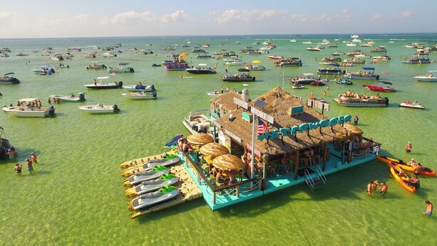 Un restaurant flottant, doté d’un toit de chaume, entouré de nombreux bateaux sur une eau verte et limpide.