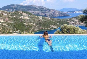 A woman in a swimming pool with a mountainous landscape in the background. - Villa Luxe - Infinity Pool With Breathtaking Views of The Ionian Sea (Lefkada)