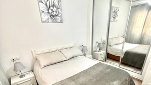 Un dormitorio con una cama, mesitas de noche, una lámpara, un espejo y una obra de arte en la pared.