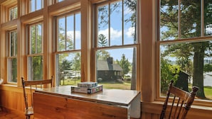 A wooden desk with a puzzle box, two chairs, and large windows with a view of a house and trees. - Saddleback Lake Lodge 02 | Close to Saddleback (Rangeley)
