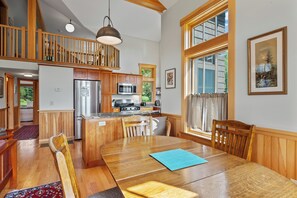 Une cuisine spacieuse dotée de meubles en bois, d’un réfrigérateur en acier inoxydable et d’un four à micro-ondes. On y trouve également un coin repas avec une table et des chaises en bois, ainsi qu’une grande fenêtre qui laisse entrer la lumière naturelle.