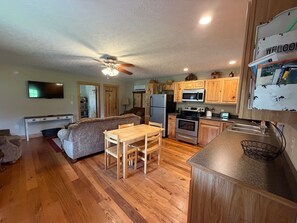 A compact kitchen with wooden cabinets, a microwave, a refrigerator, and a dining area with a table and chairs.