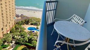 Un balcon avec une table et des chaises donnant sur une plage et une piscine.