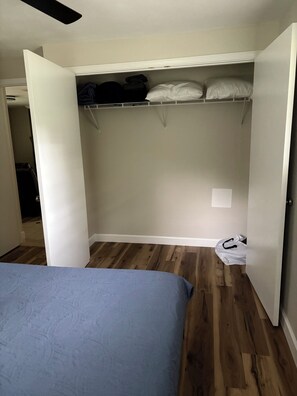 Une chambre à coucher avec un lit, un plancher en bois, un placard avec des étagères et un ventilateur de plafond.