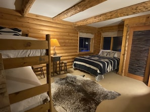 A cabin-style bedroom with a bunk bed, a single bed, a desk with a lamp, and a large fur rug.