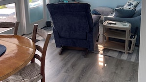 A living room with a ceiling fan, a flat-screen TV, a blue couch, a wooden dining table with chairs, and a window with blinds. - NEW FOR THIS SEASON BACK UP BATTERIES. NO WAPA NO PROBLEM (St John)