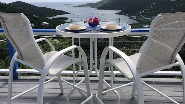 A table with two chairs on a balcony overlooking a bay with boats and hills. - NEW FOR THIS SEASON BACK UP BATTERIES. NO WAPA NO PROBLEM (St John)