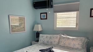 A bedroom with a bed, a ceiling fan, a wall-mounted air conditioner, a framed picture, and a window with blinds. - NEW FOR THIS SEASON BACK UP BATTERIES. NO WAPA NO PROBLEM (St John)