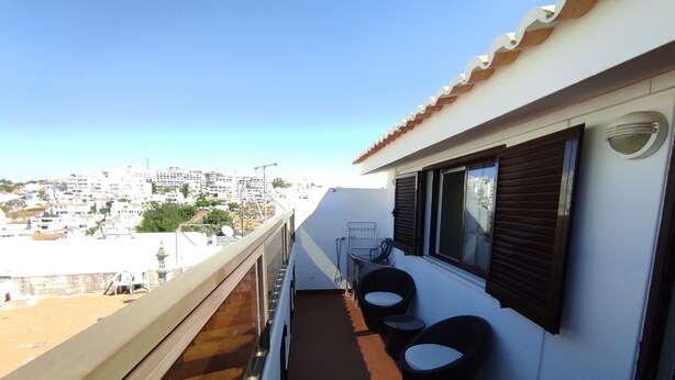 Un balcon offrant une vue sur le paysage urbain, avec une balustrade, deux chaises et une petite table.