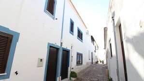 Une ruelle pavée étroite, bordée de bâtiments blancs aux volets et aux encadrements bleus.