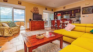 A living room with a yellow sofa, wooden coffee table, and a TV. There's a dining area with chairs and a table, and a kitchen area with a microwave and stove. - Beach front home in Zaboric (Zaboric)