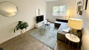 A modern living room with a flat-screen TV, a sofa, a coffee table, a lamp, and a potted plant. - Private Stylish Apartment in Cole Valley (San Francisco)