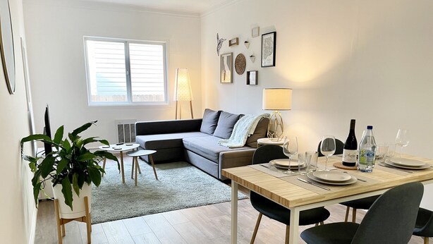 A modern living room with a sofa, a dining table set for two, and a potted plant. - Private Stylish Apartment in Cole Valley (San Francisco)