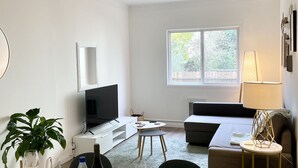 A modern living room with a dining area, a flat-screen TV, a sofa, and a lamp. - Private Stylish Apartment in Cole Valley (San Francisco)