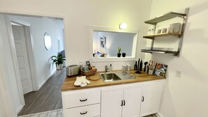 A modern kitchen with white cabinetry, a wooden countertop, a built-in sink, and a window above the sink. - Private Stylish Apartment in Cole Valley (San Francisco)
