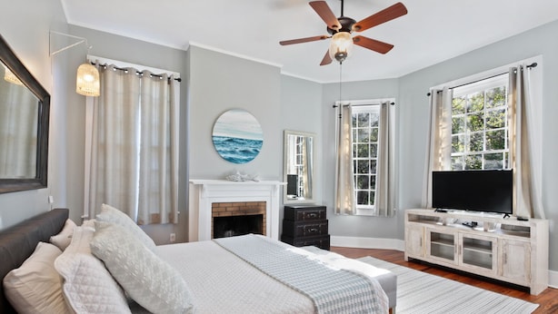 A bedroom with a bed, a fireplace, a television, and a ceiling fan.