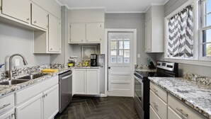 A modern kitchen with white cabinetry, granite countertops, a built-in oven, and a coffee maker.