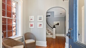 A hallway with a wicker chair, a staircase, and framed pictures on the wall.