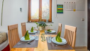 Una tavola da pranzo imbandita per quattro, con sedie di legno, un vaso con fiori e una finestra vista alberi.