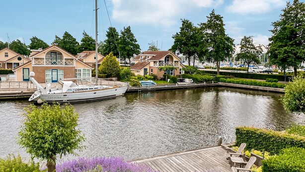 A canal with a docked boat, houses, and a wooden deck with chairs. - 3 bedroom luxurious home in Workum (Workum)