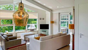 A modern living room with a large window, a hanging light fixture, a television, and a sofa. - 3 bedroom luxurious home in Workum (Workum)