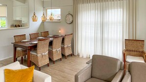 A dining area with a wooden table and wicker chairs, a sofa with a yellow pillow, and a large window with curtains. - 3 bedroom luxurious home in Workum (Workum)