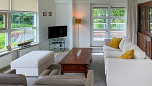 A modern living room with a sofa, ottoman, coffee table, and a television. - 3 bedroom luxurious home in Workum (Workum)