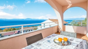 A balcony with a table set for two, overlooking a coastal view with mountains in the distance. - Nice apartment in Njivice with WiFi (Njivice)
