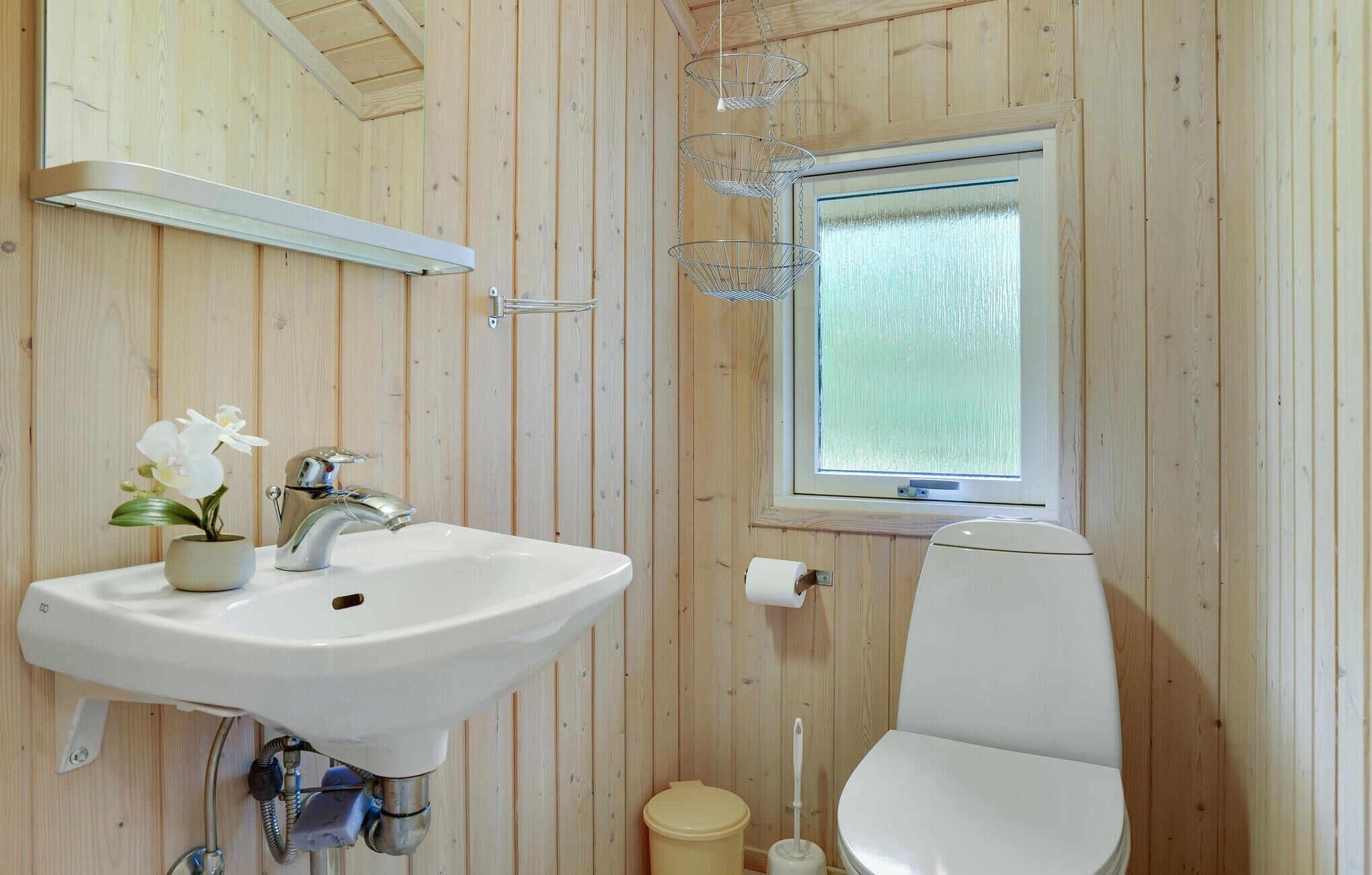 A wooden-paneled bathroom with a white sink, toilet, and window.