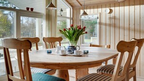 Une table de salle à manger en bois, avec des chaises, un vase rempli de tulipes rouges et une carafe.