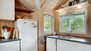 Une cuisine avec des meubles en bois, un réfrigérateur blanc, un évier et une fenêtre donnant sur des arbres.