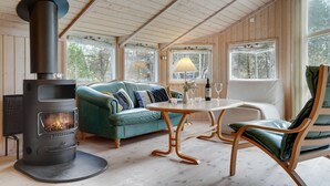 L’intérieur d’un chalet accueillant, avec un poêle à bois, un canapé vert, une table à manger en bois et une chaise.