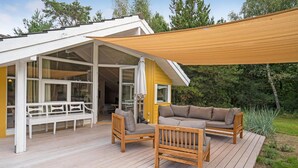 Une terrasse en bois dotée d’un espace salon couvert, d’un canapé et d’un banc.