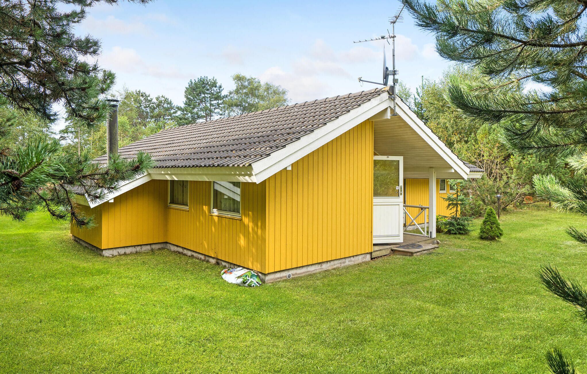 A yellow cabin with a tiled roof, a small porch, and a door.