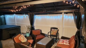 Un espacio al aire libre con patio, mobiliario de mimbre, una mesa y luces colgantes.