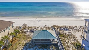 A beach view with a building featuring a blue roof and a wooden deck. - Endless Summer - Home in Prestigious Community with Gulf Views & Secluded Pool Area (Miramar Beach)
