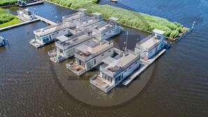 En fritliggende husbåd med flere etager, fortøjet i en stille flod.
