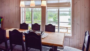 Ett matbord i trä med sex stolar, två hänglampor och utsikt över en sjö genom stora fönster.