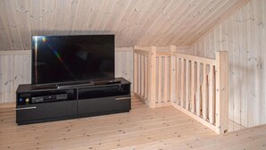 Ett rum med träpanel på väggarna, en svart möbel för underhållningssystemet och en stor tv-skärm.