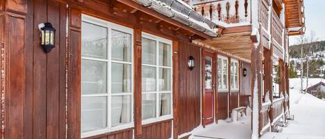 A wooden cabin with large windows, a porch, and a snow-covered exterior.