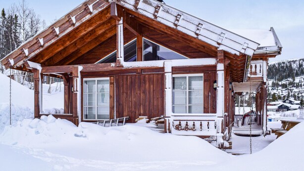 En stuga byggd av trä med ett sluttande tak, stora fönster och en veranda.