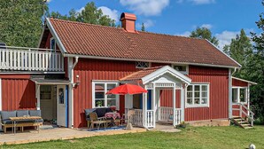 Ett rött trähus med ett tak täckt av takpannor, en veranda med ett rött parasoll och en liten terrass med utemöbler.