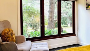 A room with a large window, a beige armchair, a white sofa, and a yellow throw pillow. - The Yellow Feather Cottage - Enchanting & Private Romantic Stay! (Wentworth Falls)