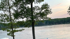 Blick auf einen See mit Steg, Booten und einer Rasenfläche mit Außenbestuhlung.