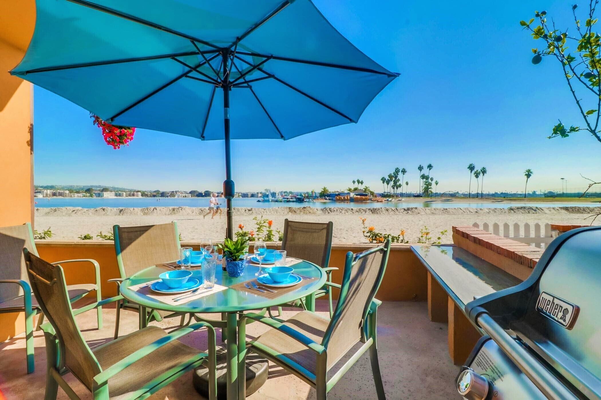Une terrasse avec une table dressée pour deux personnes, un barbecue et une vue sur la plage.