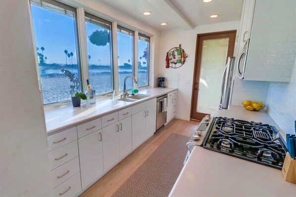 A kitchen with white cabinets, a stainless steel sink, and a gas stove. - Stay Waterfront on Mission Bay, Just Steps from the Ocean (San Diego)