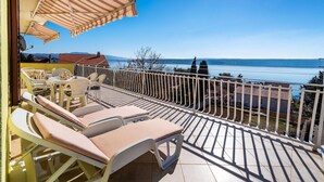 Een balkon met loungestoelen, een gestreept zonnescherm en uitzicht op de zee en verre bergen.