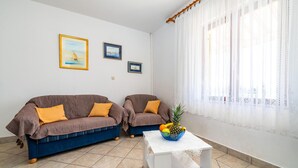 Een woonkamer met twee gestreepte banken, een kleine witte tafel met een fruitschaal, en twee ingelijste foto's aan de muur.
