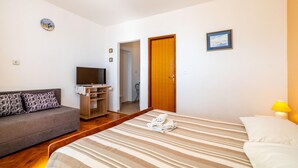 Een slaapkamer met een bed, een televisie op een houten standaard, een bank, een deur en een klein schilderij aan de muur.